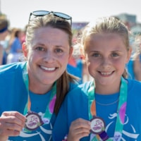 Girls on the Run participant holding program 5K medal with coach.